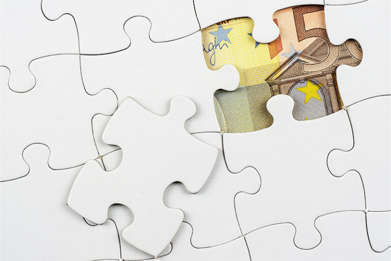 Ein Puzzle, bei dem nur ein Puzzlestück fehlt, durch dessen Lücke ein Geldschein sichtbar ist.