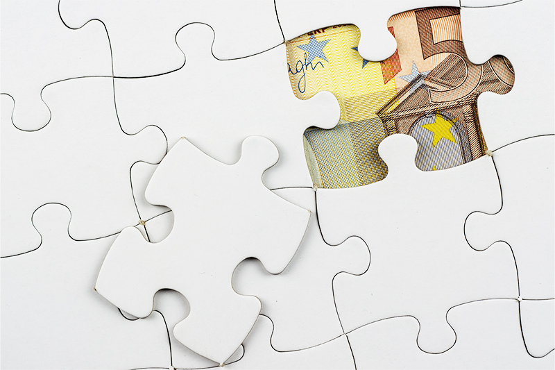 Ein Puzzle, bei dem nur ein Puzzlestück fehlt, durch dessen Lücke ein Geldschein sichtbar ist.